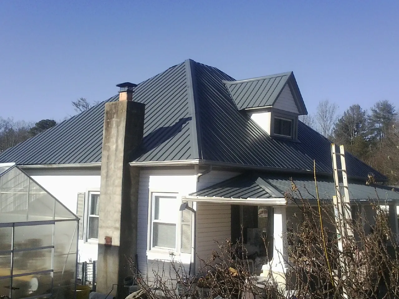 Dark blue standing seam metal roof on a white farmhouse with dormer — Slate & Tile Roof Repair by Roofing Brothers in Buckhead