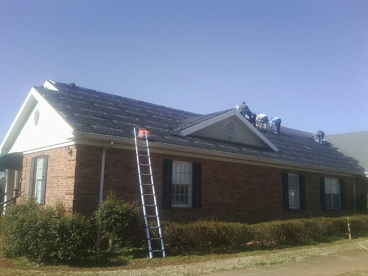 Crew tearing shingles off a brick ranch roof with a ladder set — Emergency Roof Repair work by our crew in Buckhead
