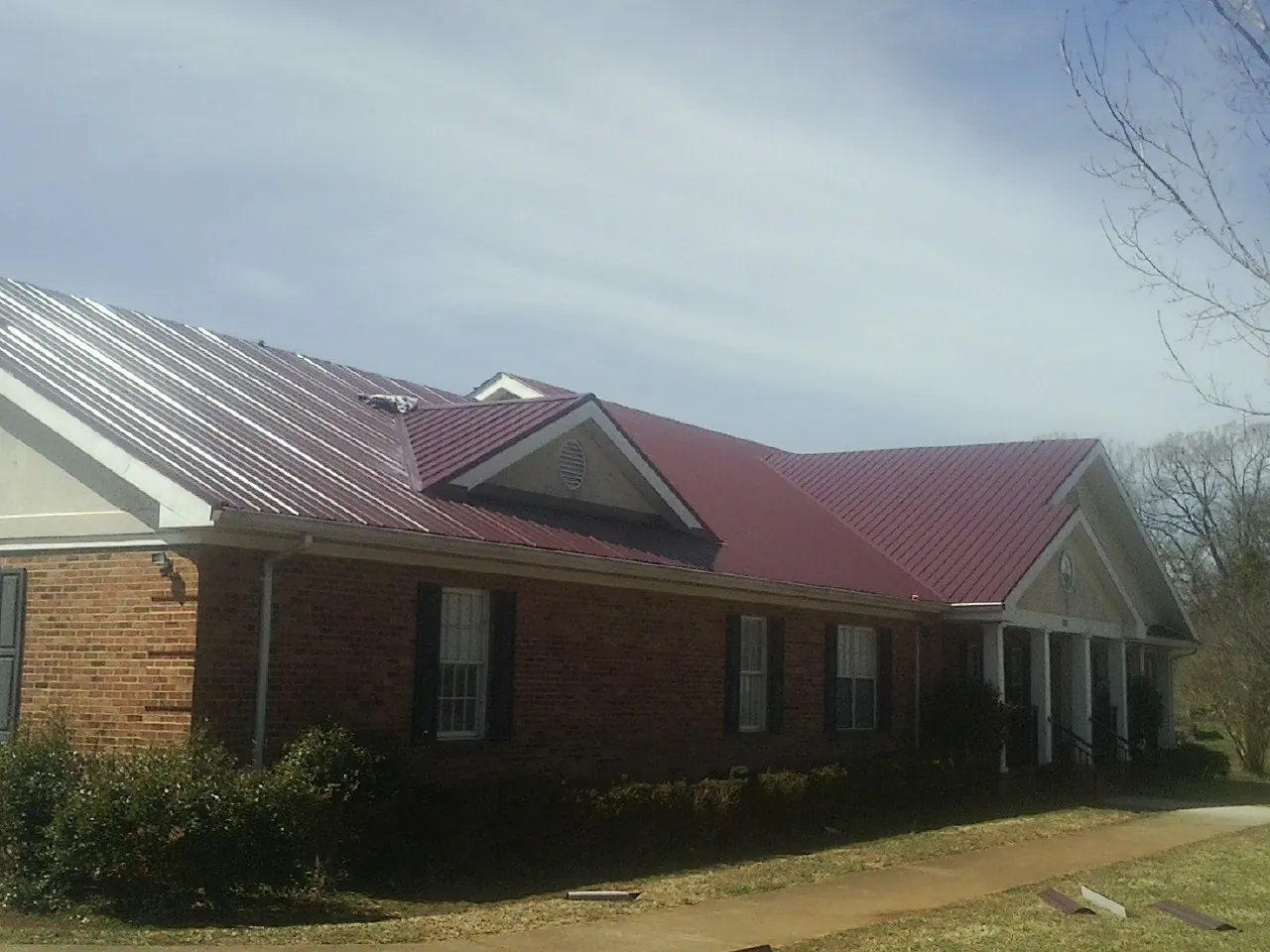 Red metal roof with gabled entries on a long brick building, from a Hail Damage Roof Repair job in Buckhead