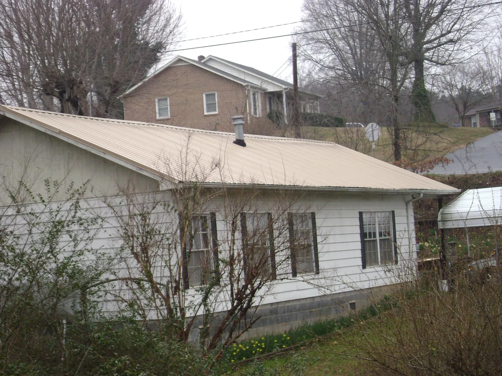 Tan metal roof on a white sided house set into a hillside — Commercial Roofing by Roofing Brothers in Buckhead